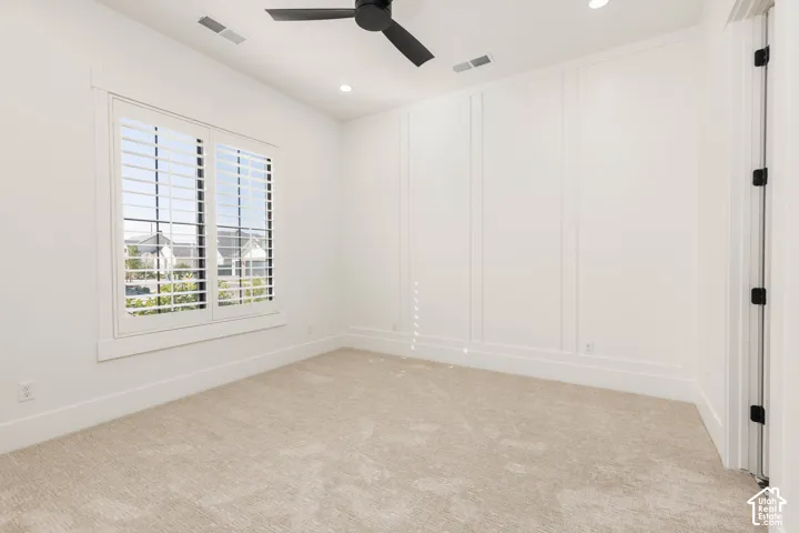 Recessed lighting, ceiling fan, accent wall paneling, window with plantation shutters, and light-toned carpeting