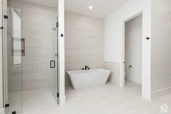 Freestanding soaking tub, glass-enclosed shower with built-in shelf, large format tile flooring, and matching wall tile accents