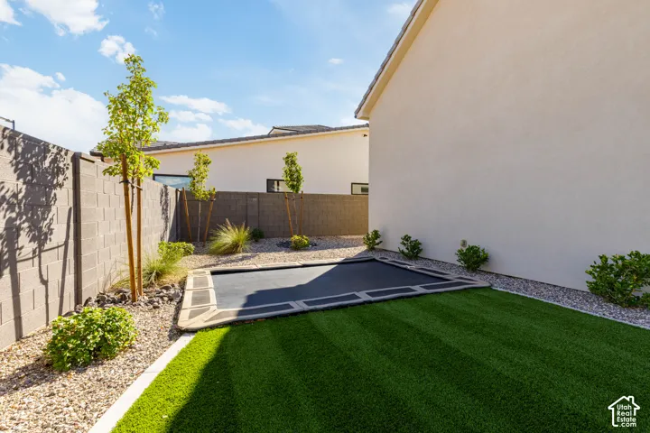 Low-maintenance backyard featuring artificial turf, gravel landscaping, a block wall, and mature plantings