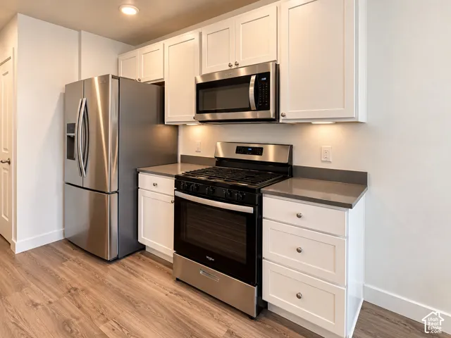 Kitchen featuring stainless steel appliances, white cabinetry, solid surface countertops, under-cabinet lighting, and wood-finish flooring