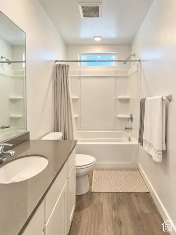 White vanity with a single basin sink, grey countertop, wood-finish flooring, white bathtub with a shower, and an overhead window