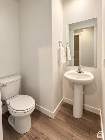 Pedestal sink with chrome faucet, wall-mounted mirror, wood-finish flooring, and white toilet