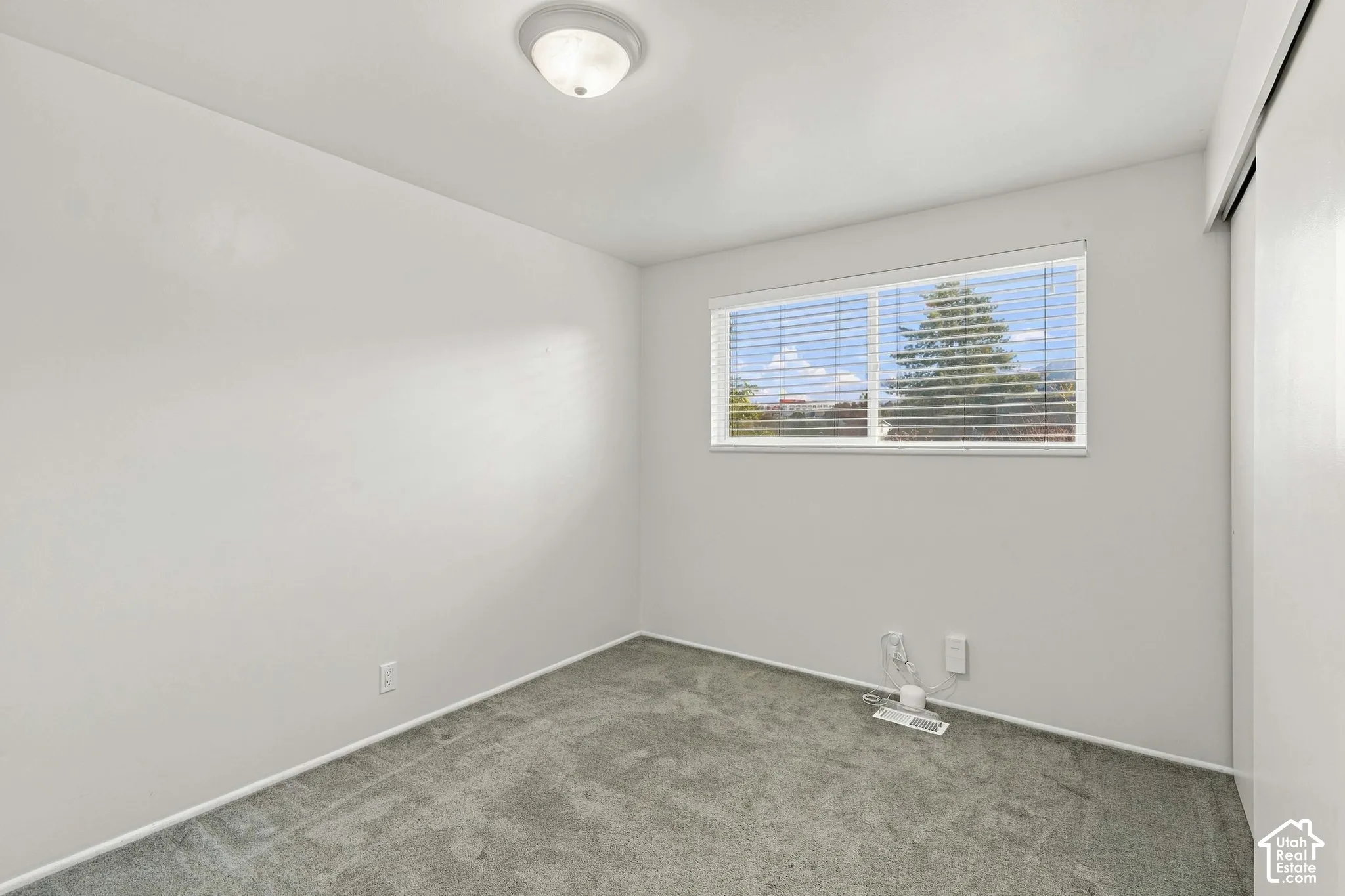 Recessed window with blinds, overhead flush mount lighting, and gray carpet flooring