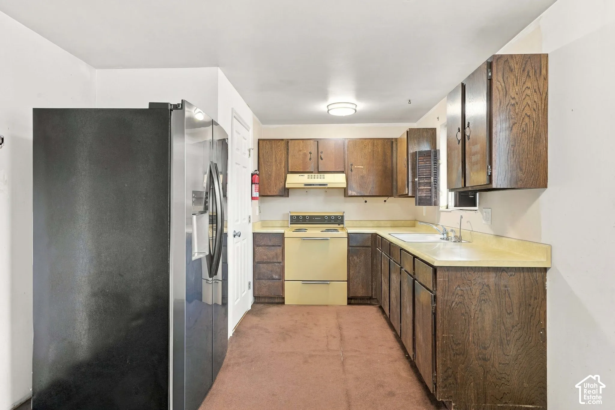Kitchen featuring wood cabinetry, laminate countertops, a built-in sink, and a range with an overhead hood