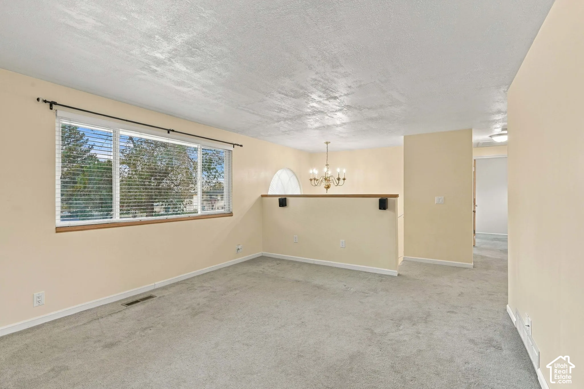 Bright living area with a large window, neutral carpeting, and a half-wall partition