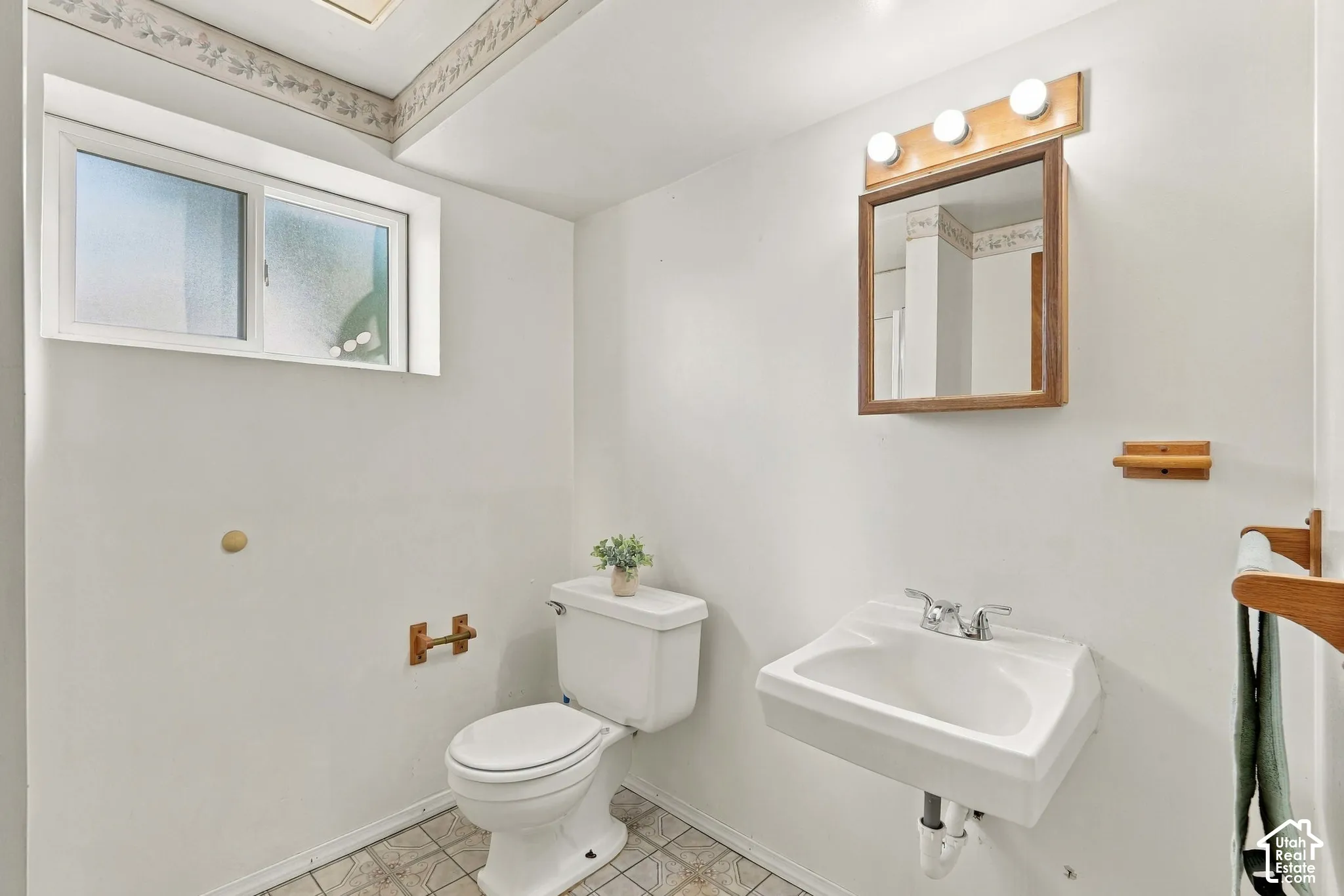 Wall-mounted vanity sink, framed mirror with integrated lighting, and white toilet