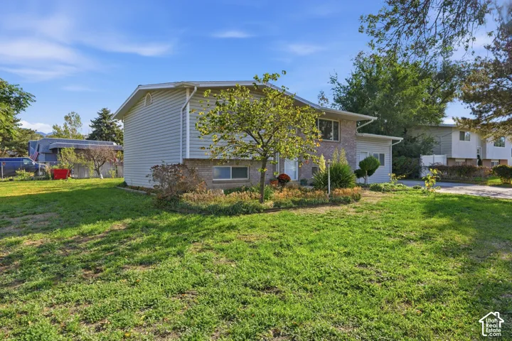 Exterior featuring light gray siding, brick accents, and a landscaped front yard with mature plantings