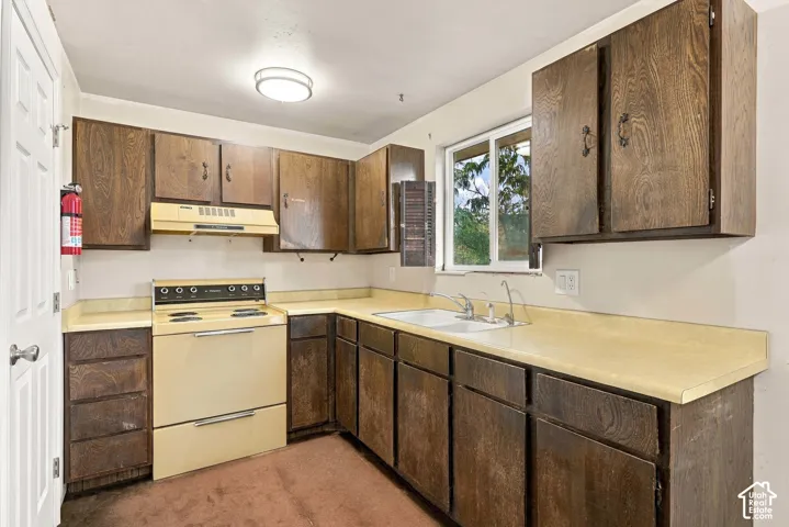 Kitchen featuring wood-finish cabinetry, a window over the sink, and a built-in electric range with a range hood