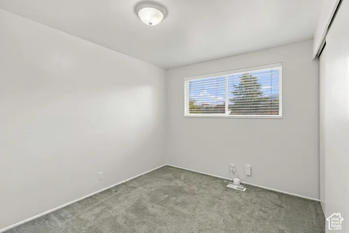 Recessed window with blinds, overhead flush mount lighting, and gray carpet flooring