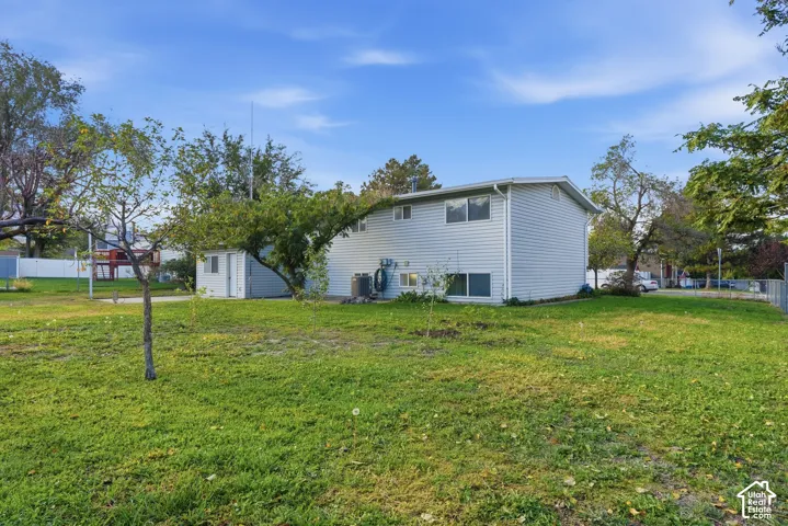Expansive grassy area with mature trees, a detached storage shed, and durable vinyl siding