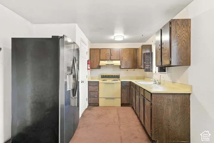Kitchen featuring wood cabinetry, laminate countertops, a built-in sink, and a range with an overhead hood