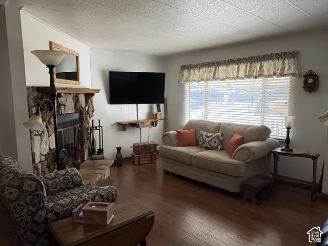 Wood-finish flooring, stone-clad fireplace with wood mantel, large window with horizontal blinds, and white paneling accents