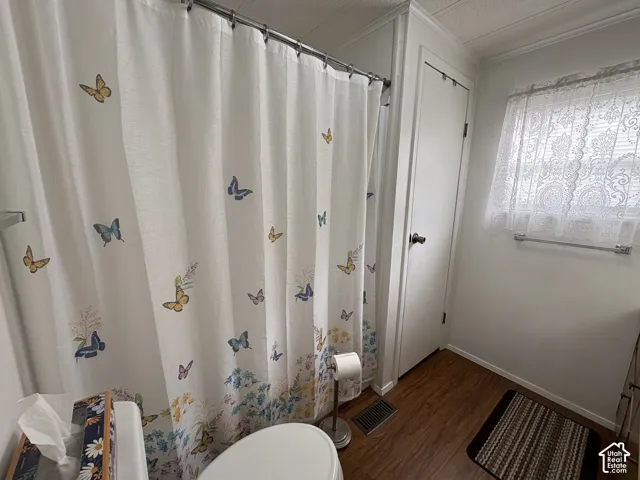 Wood-finish flooring with white baseboards, a white wall, and a white interior door