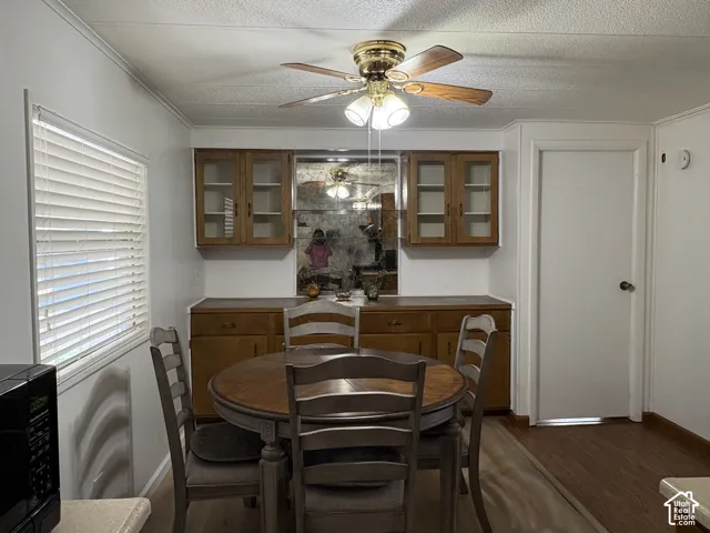 Built-in wood-finish cabinetry featuring glass-front upper cabinets, brass ceiling fan with integrated lighting, wood-finish flooring, and white window blinds