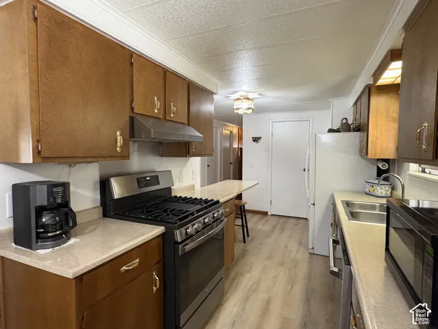 Kitchen featuring wood-finish cabinetry, stainless steel range with hood, double basin sink, and light-toned countertops