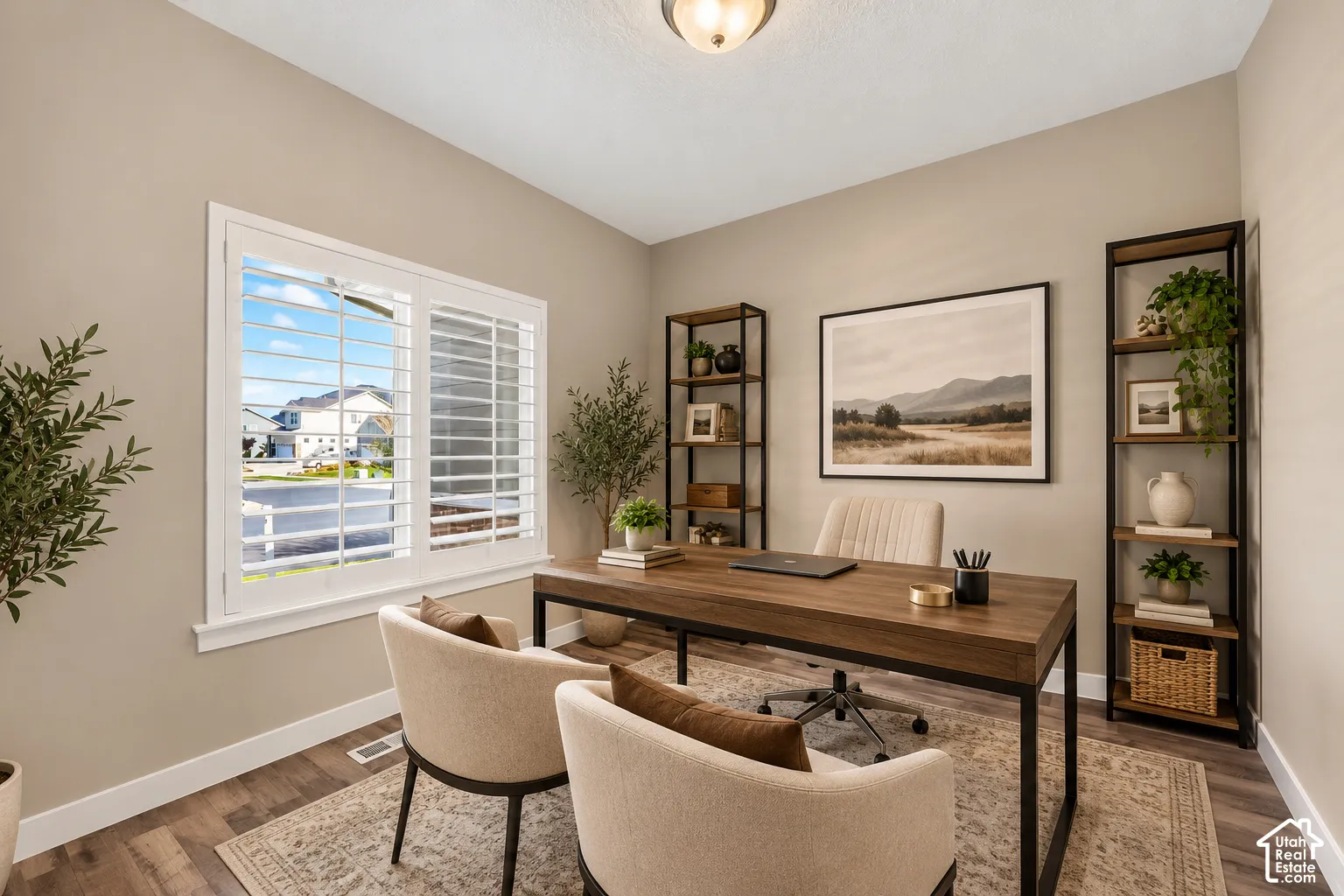 Dedicated home office featuring a wood-finish desk, built-in shelving with display cubbies, large multi-pane windows with plantation shutters, neutral wall finishes, and area rug flooring detail