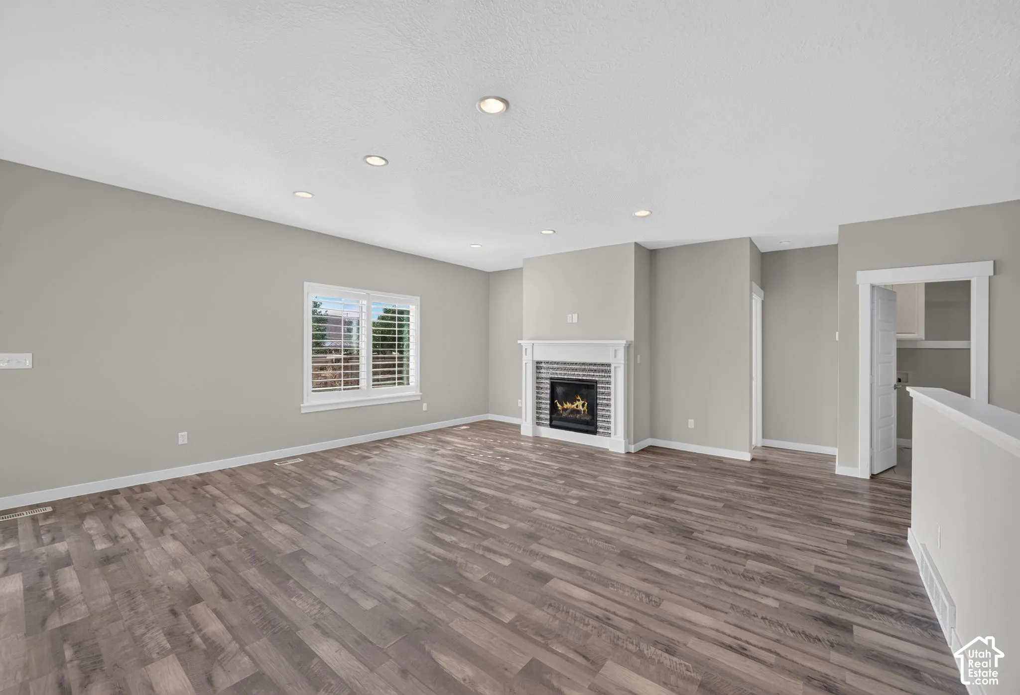 Spacious room featuring wood-finish flooring, recessed lighting, a fireplace with a decorative mantel and tile surround, and window shutters