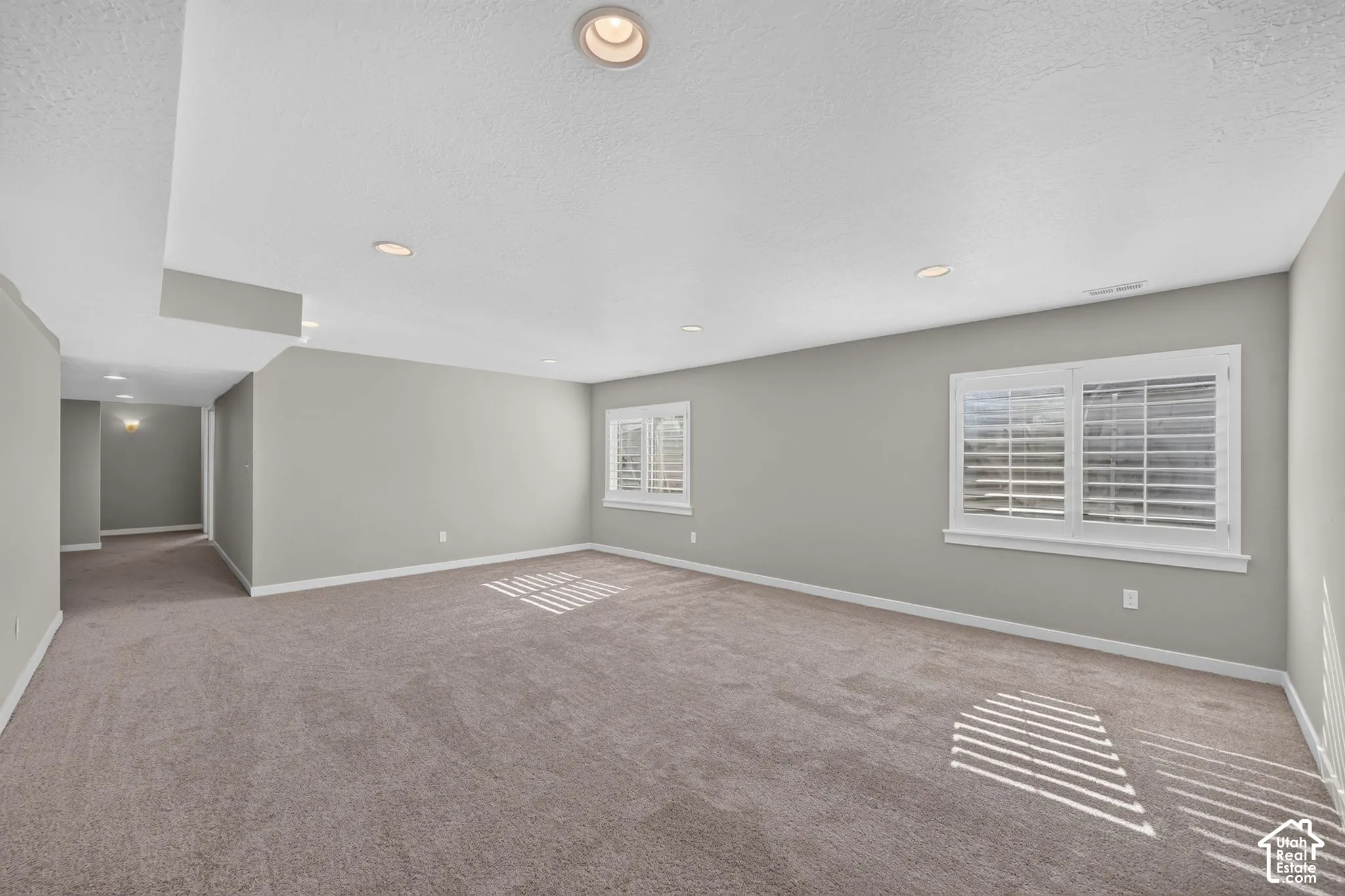 Spacious room with carpet flooring, recessed lighting, neutral wall paint, and white plantation shutters on windows