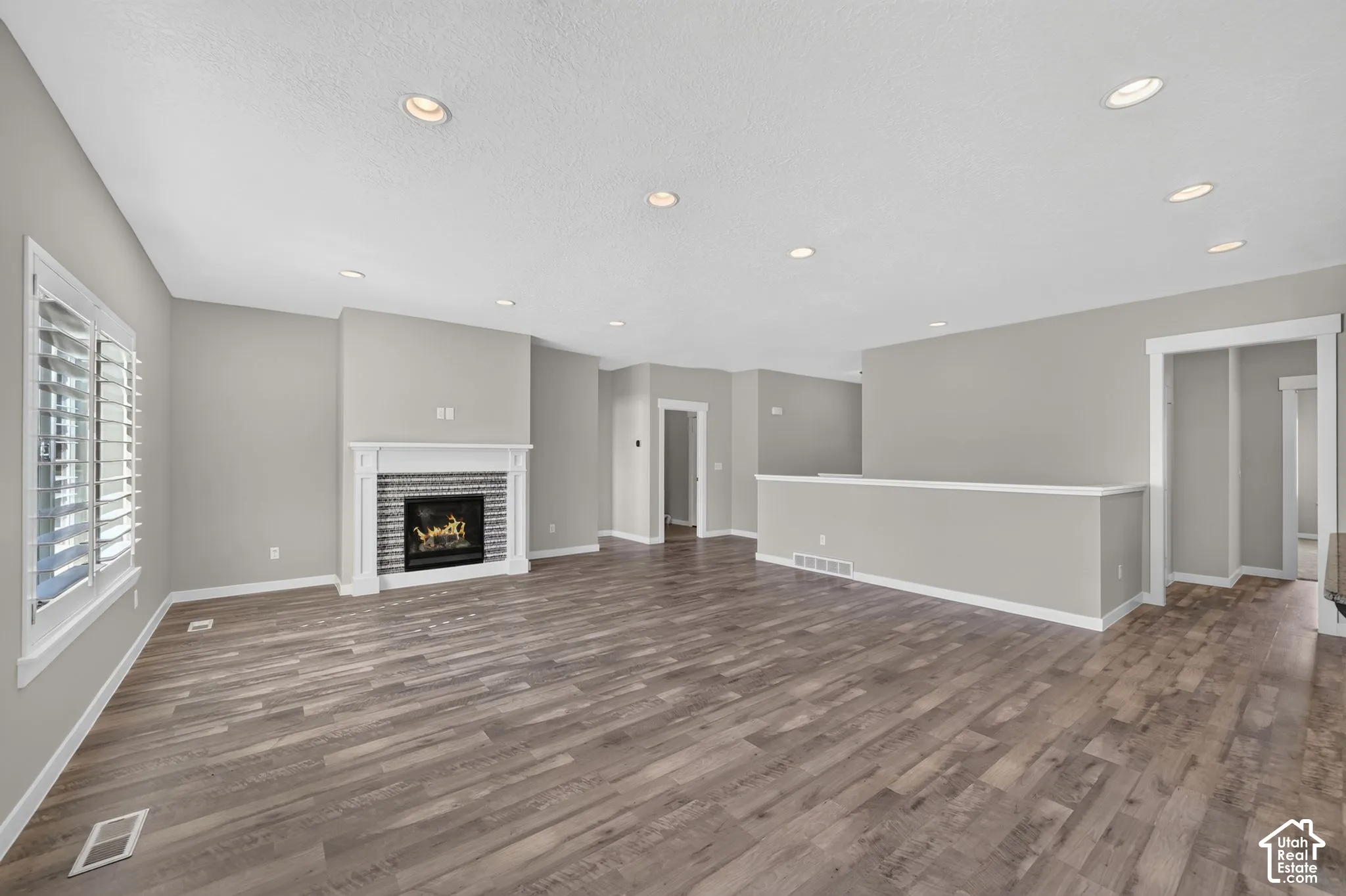Recessed lighting, wood-finish flooring, white plantation shutters, fireplace with tile surround, and white trim throughout