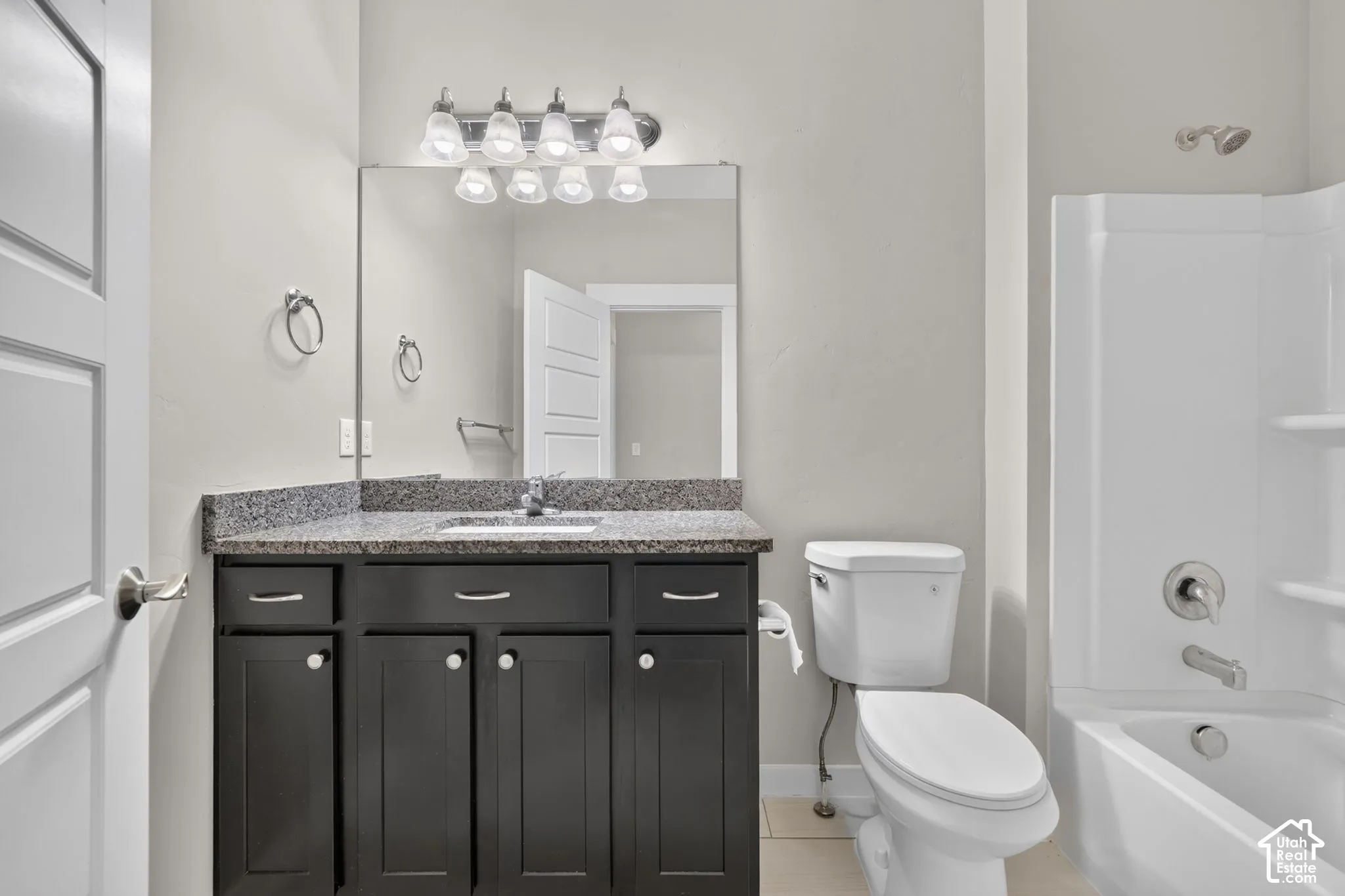 Bathroom featuring a dark wood vanity with a granite-look countertop, a rectangular mirror, a light fixture with multiple bulbs, and a white tub/shower combination