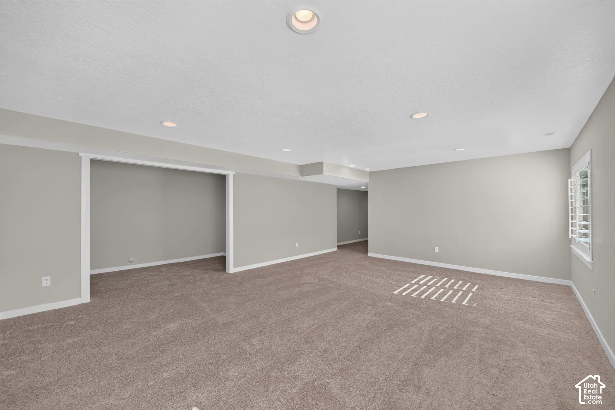 Recessed ceiling lighting, neutral-toned carpeting, light gray wall paint, white trim, and a window with plantation shutters