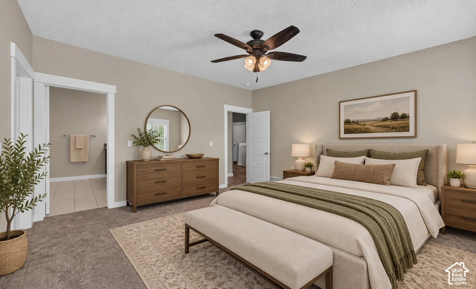 Primary bedroom suite featuring a wood-finish dresser with circular mirror, ceiling fan with integrated lighting, neutral wall-to-wall carpeting, and en-suite bathroom access