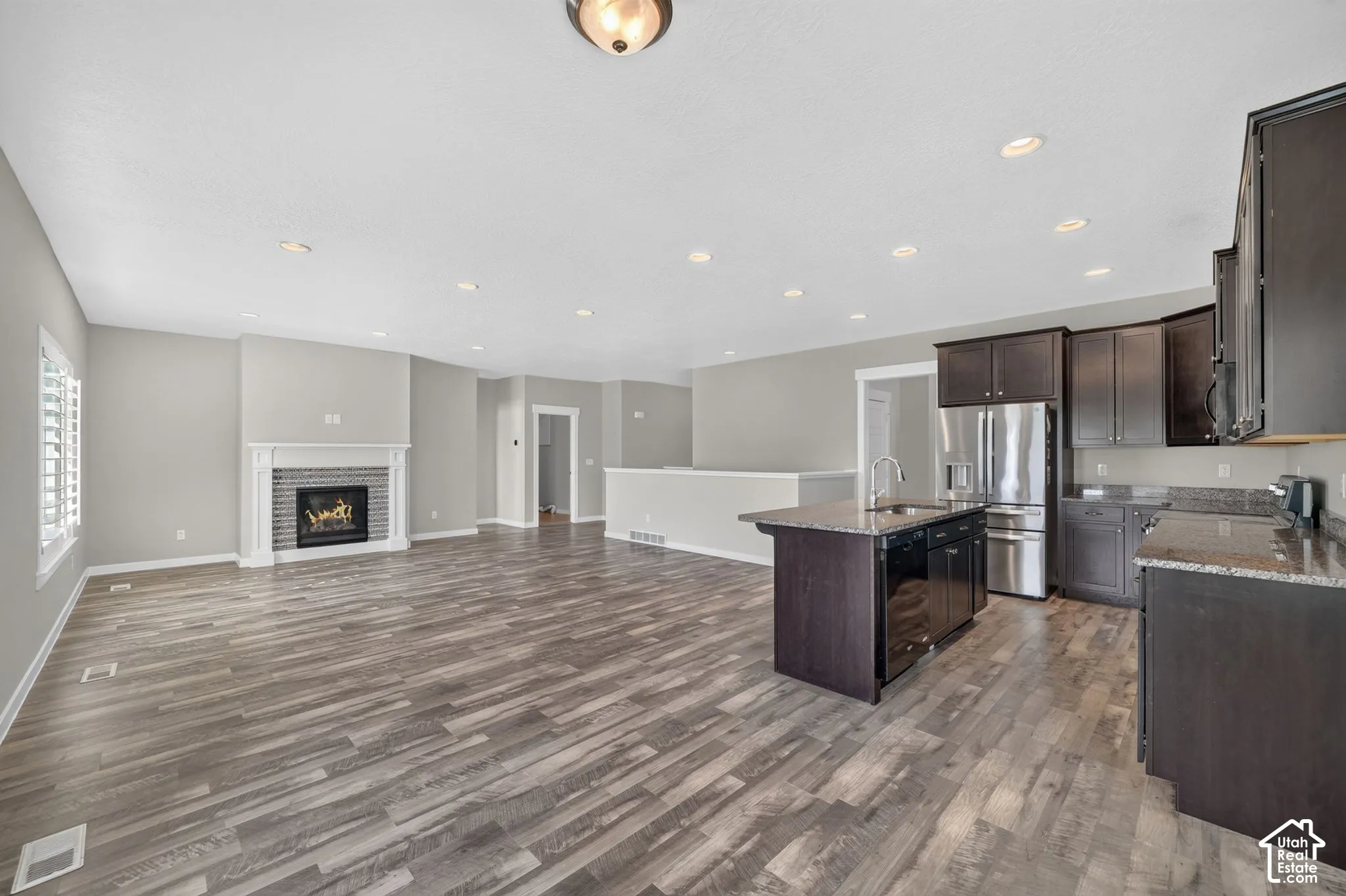 Open-concept living space featuring wood-finish flooring, a fireplace with a white mantel and gray tile surround, and recessed lighting