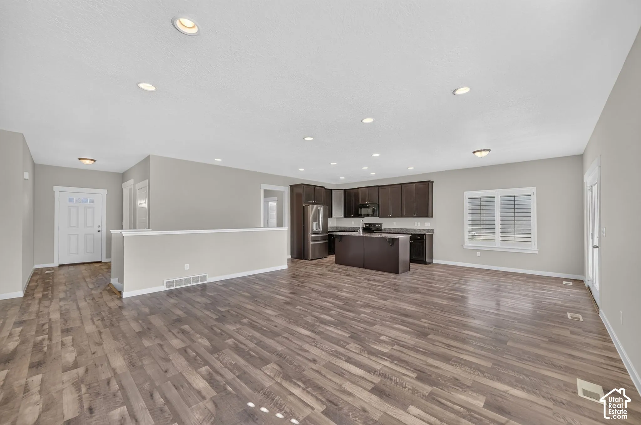 Wood-finish flooring throughout, recessed lighting, kitchen with dark wood cabinetry, stainless steel appliances, and a central island