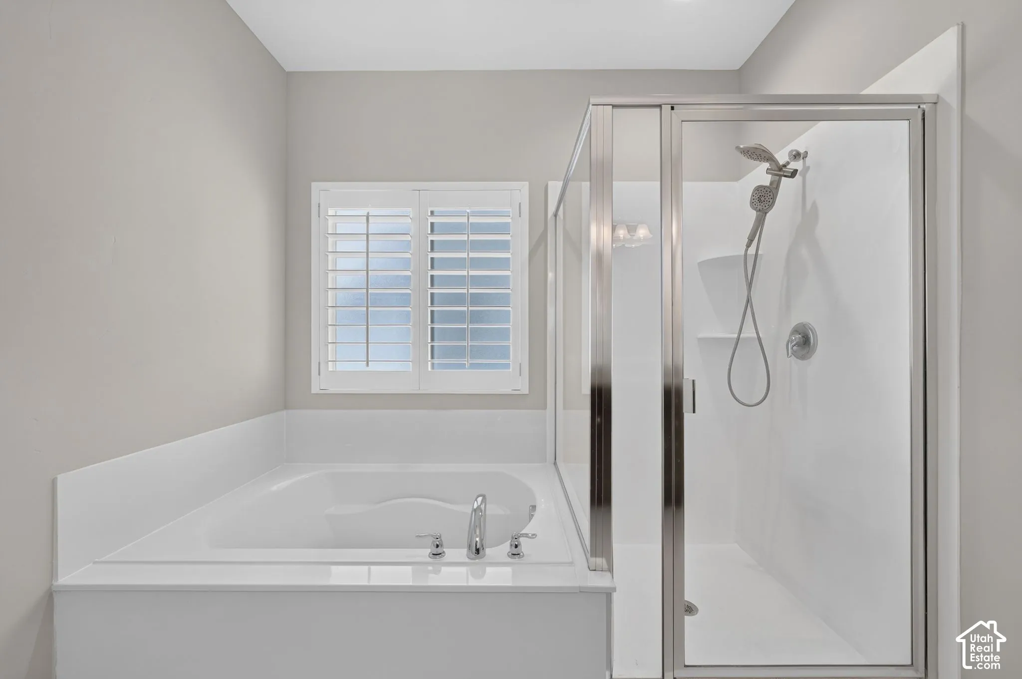 Built-in soaking tub with chrome fixtures, glass-enclosed shower with handheld showerhead, and white window shutters