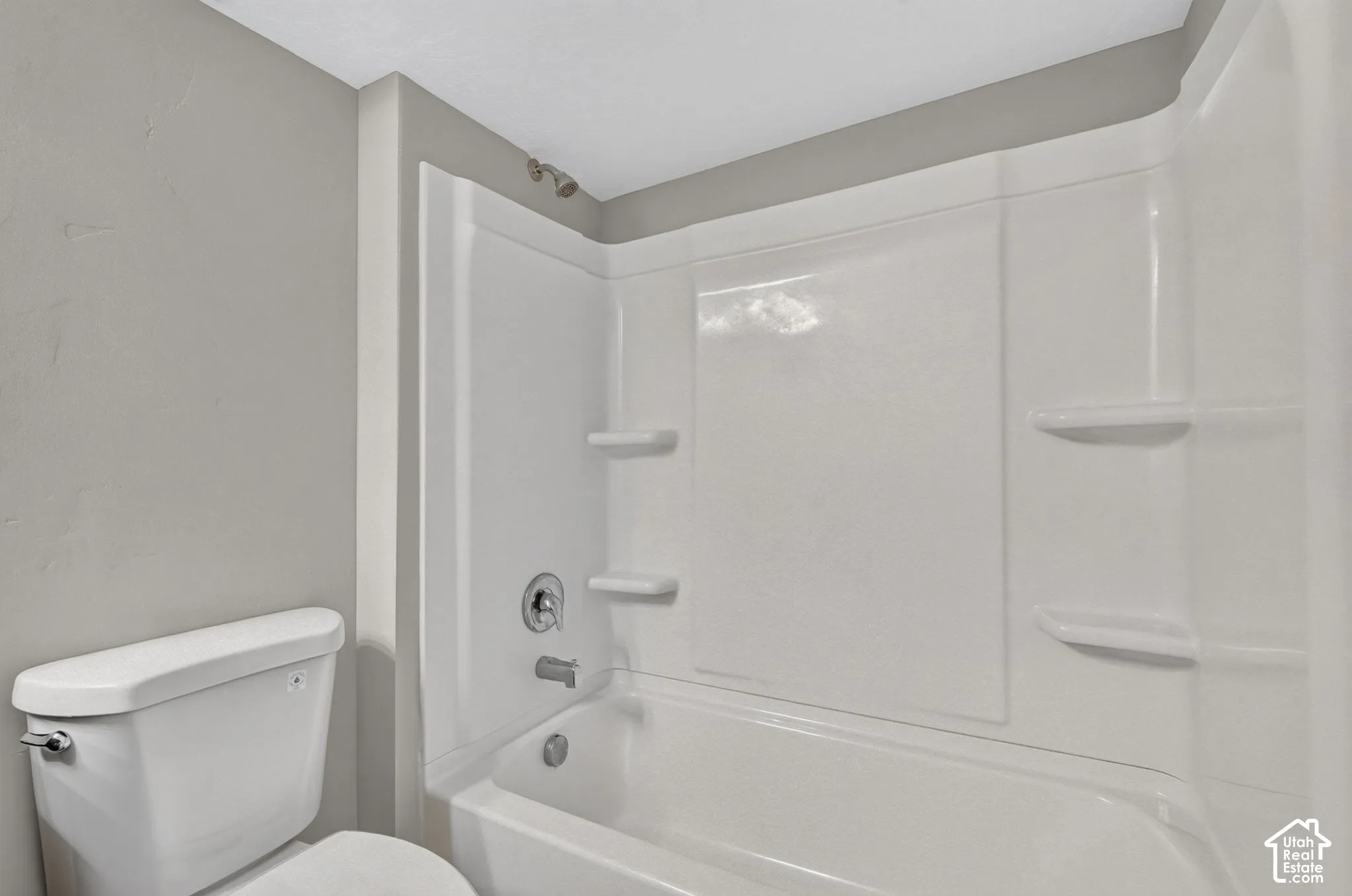 Bathtub and shower combination with a bright white surround, integrated shelving, and a chrome shower fixture