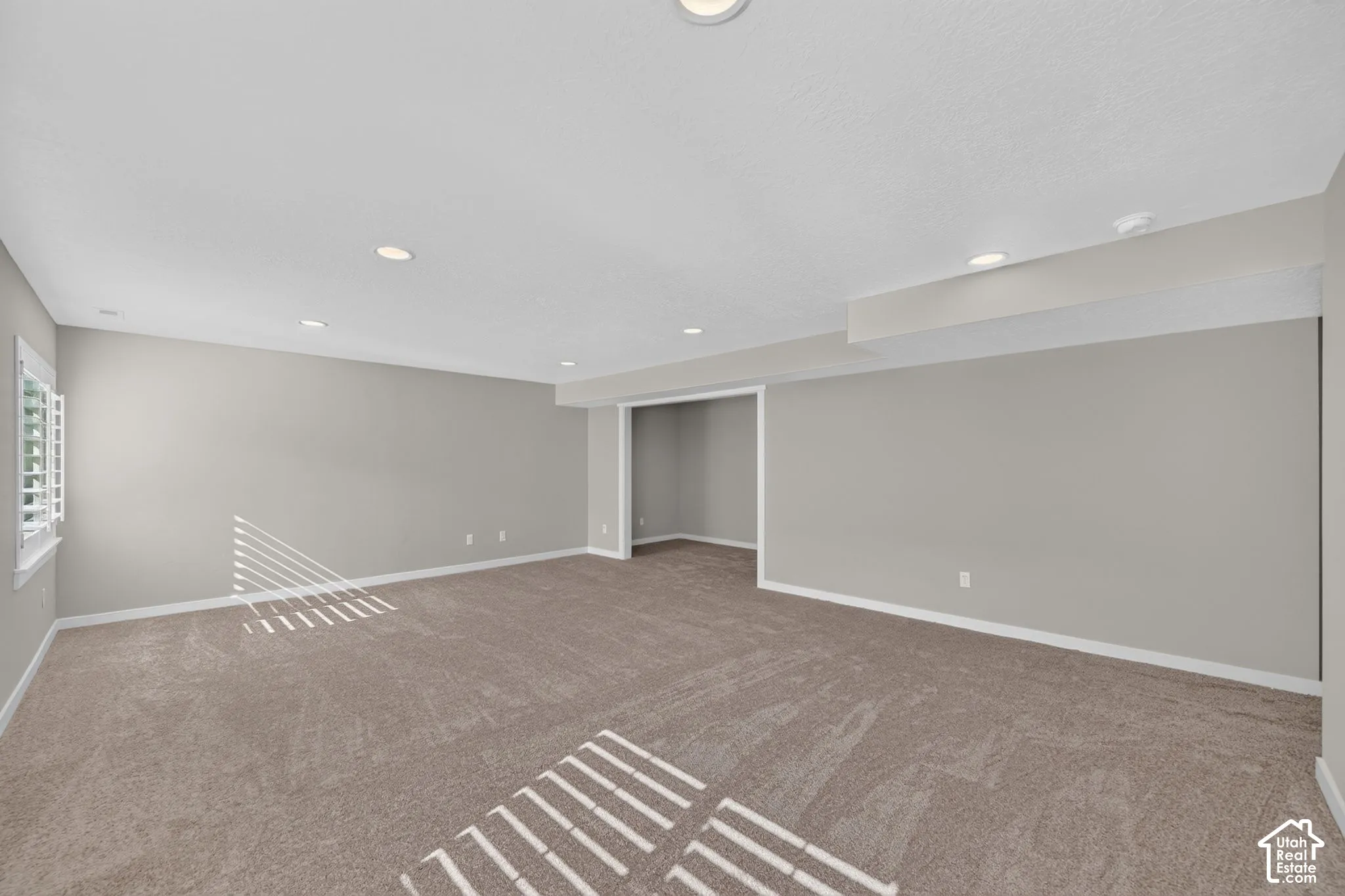 Recessed lighting, neutral gray wall tones, plush carpet flooring, white trim, and a window with plantation shutters