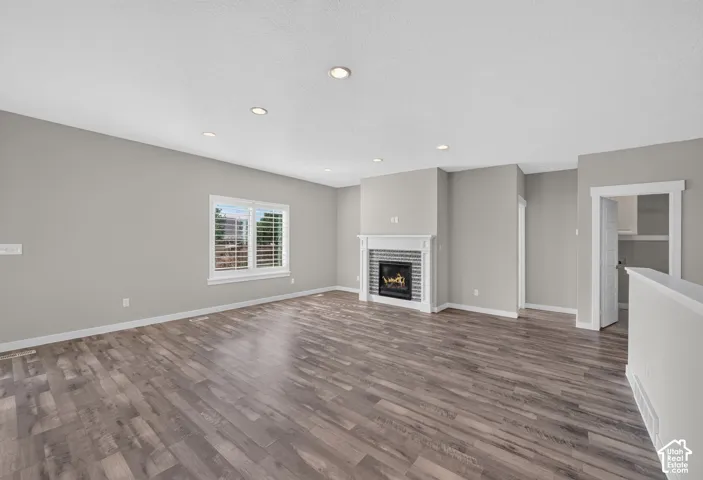 Spacious room featuring wood-finish flooring, recessed lighting, a fireplace with a decorative mantel and tile surround, and window shutters