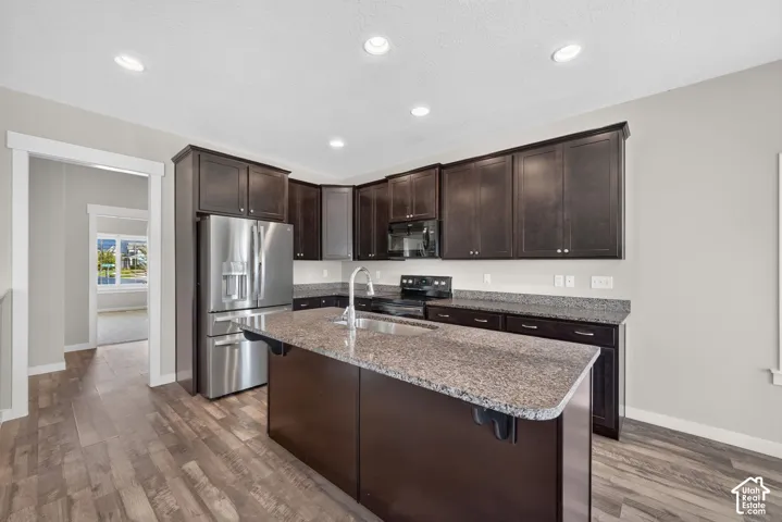 Kitchen featuring wood-finish flooring, dark wood cabinetry, stainless steel appliances, granite countertops, and recessed lighting