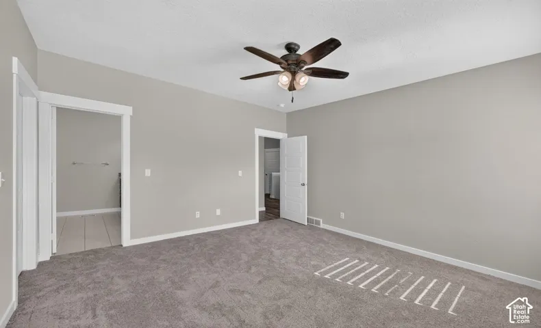 Spacious room featuring gray carpet flooring, light gray wall paint, and a ceiling fan with integrated lighting