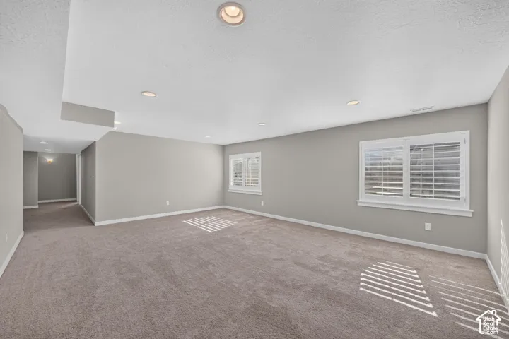 Spacious room with carpet flooring, recessed lighting, neutral wall paint, and white plantation shutters on windows