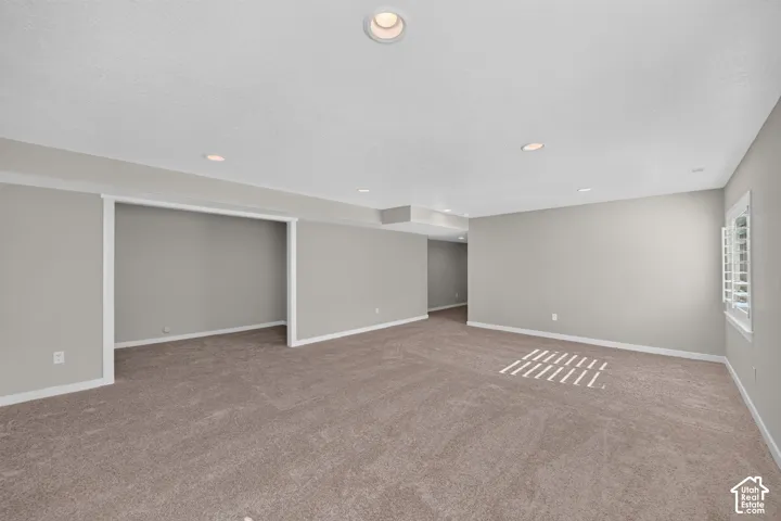 Recessed ceiling lighting, neutral-toned carpeting, light gray wall paint, white trim, and a window with plantation shutters