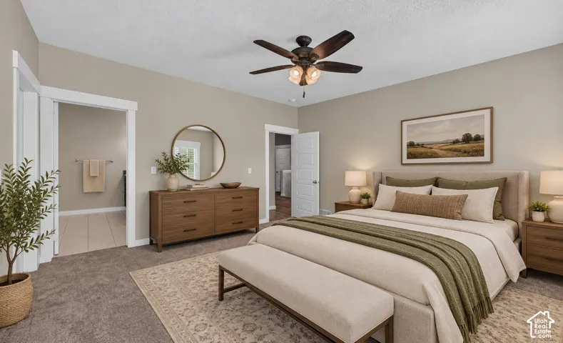 Primary bedroom suite featuring a wood-finish dresser with circular mirror, ceiling fan with integrated lighting, neutral wall-to-wall carpeting, and en-suite bathroom access