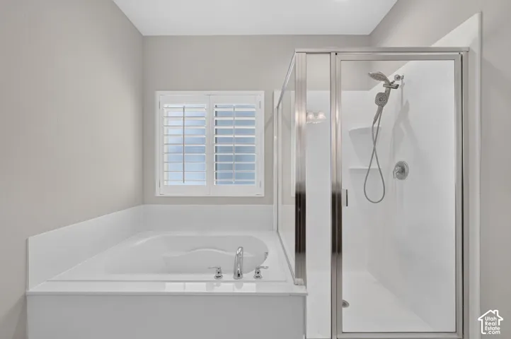 Built-in soaking tub with chrome fixtures, glass-enclosed shower with handheld showerhead, and white window shutters