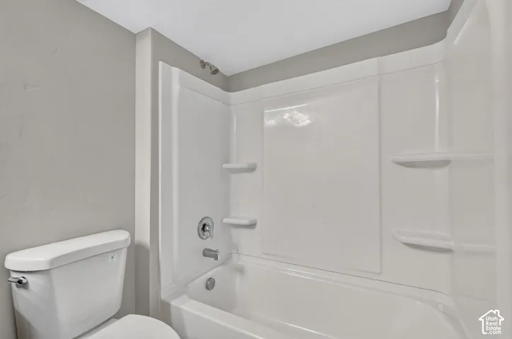 Bathtub and shower combination with a bright white surround, integrated shelving, and a chrome shower fixture