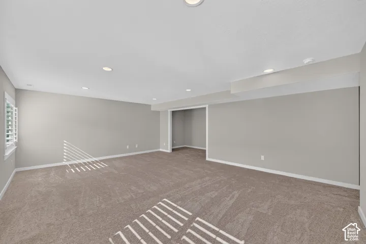 Recessed lighting, neutral gray wall tones, plush carpet flooring, white trim, and a window with plantation shutters