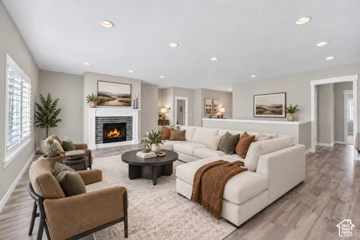 Spacious living area featuring a fireplace with stone surround and white mantle, recessed lighting, plantation shutters, and wood-finish flooring