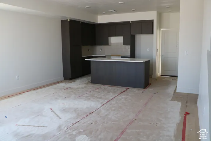 Modern kitchen featuring dark wood-finish cabinetry, a central island with a light-toned countertop, and tile backsplash