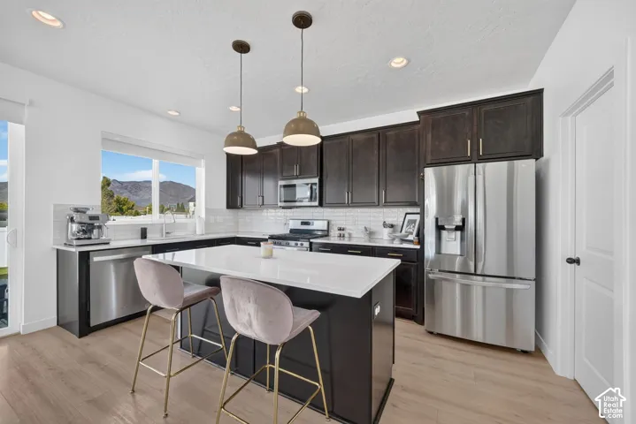 Kitchen featuring dark wood cabinetry, a center island with a light-toned countertop, stainless steel appliances all included, pendant lighting, and wood-finish flooring