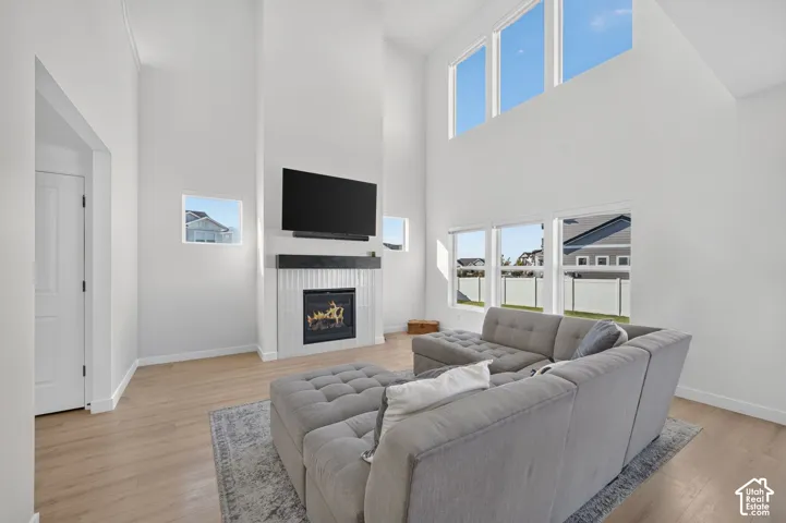 Vaulted ceilings with abundant natural light, a gas fireplace with a white tile surround, a dark wood mantel, and wood-finish flooring
