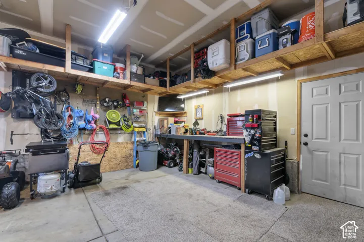Concrete flooring, built-in workbench, wall-mounted storage shelving, overhead fluorescent lighting, and a paneled interior door