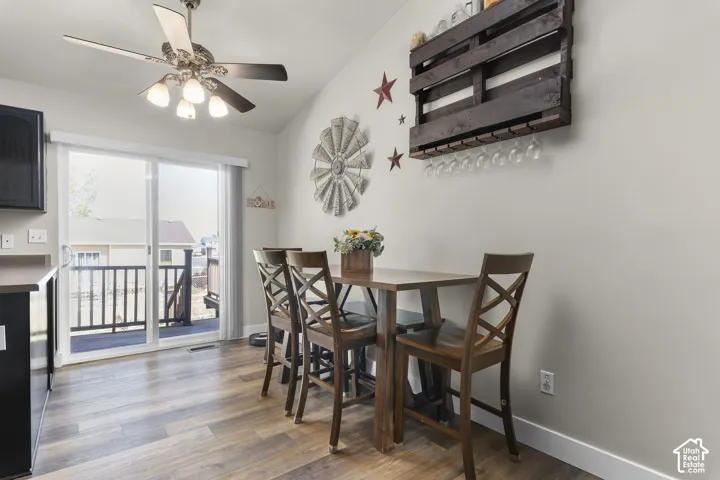 Wood-finish flooring, vaulted ceiling, ceiling fan with integrated lighting, and a sliding glass door leading to an outdoor deck