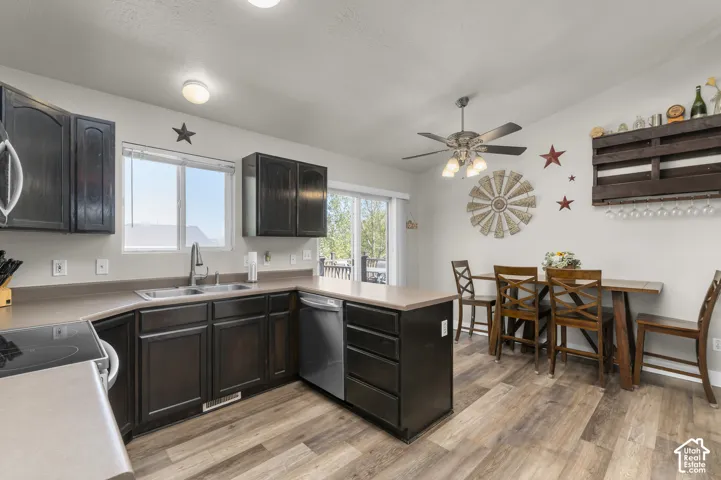 Kitchen featuring dark wood-finish cabinetry, built-in dishwasher, stainless steel sink with gooseneck faucet, light-toned countertops, and wood-finish flooring