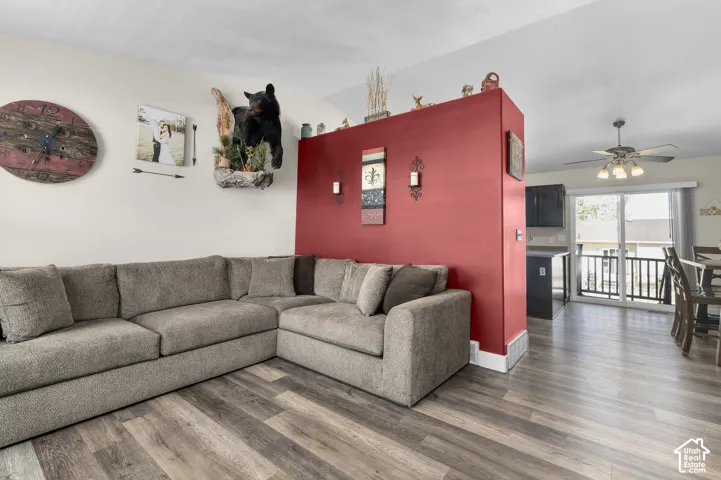 Wood-finish flooring, accent wall, ceiling fan with integrated lighting, and a sliding glass door