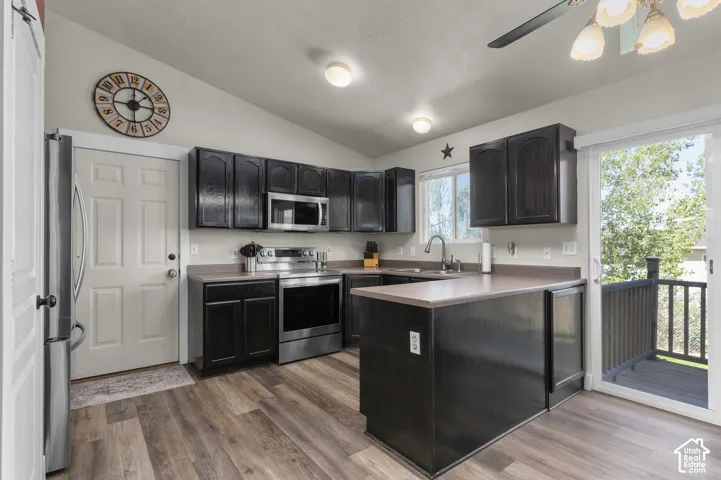 Kitchen featuring wood-finish flooring, dark cabinetry, stainless steel appliances, and a sliding glass door to an outdoor deck