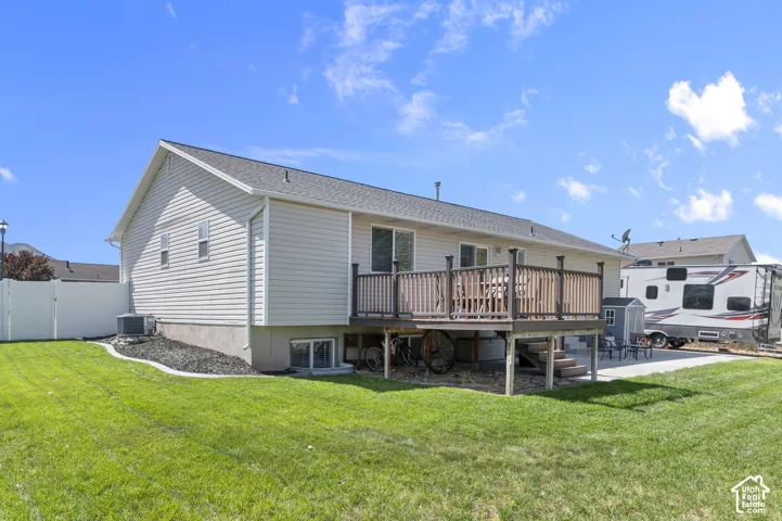 Expansive rear yard featuring a large wood deck, a concrete patio, and a side yard with a white privacy fence